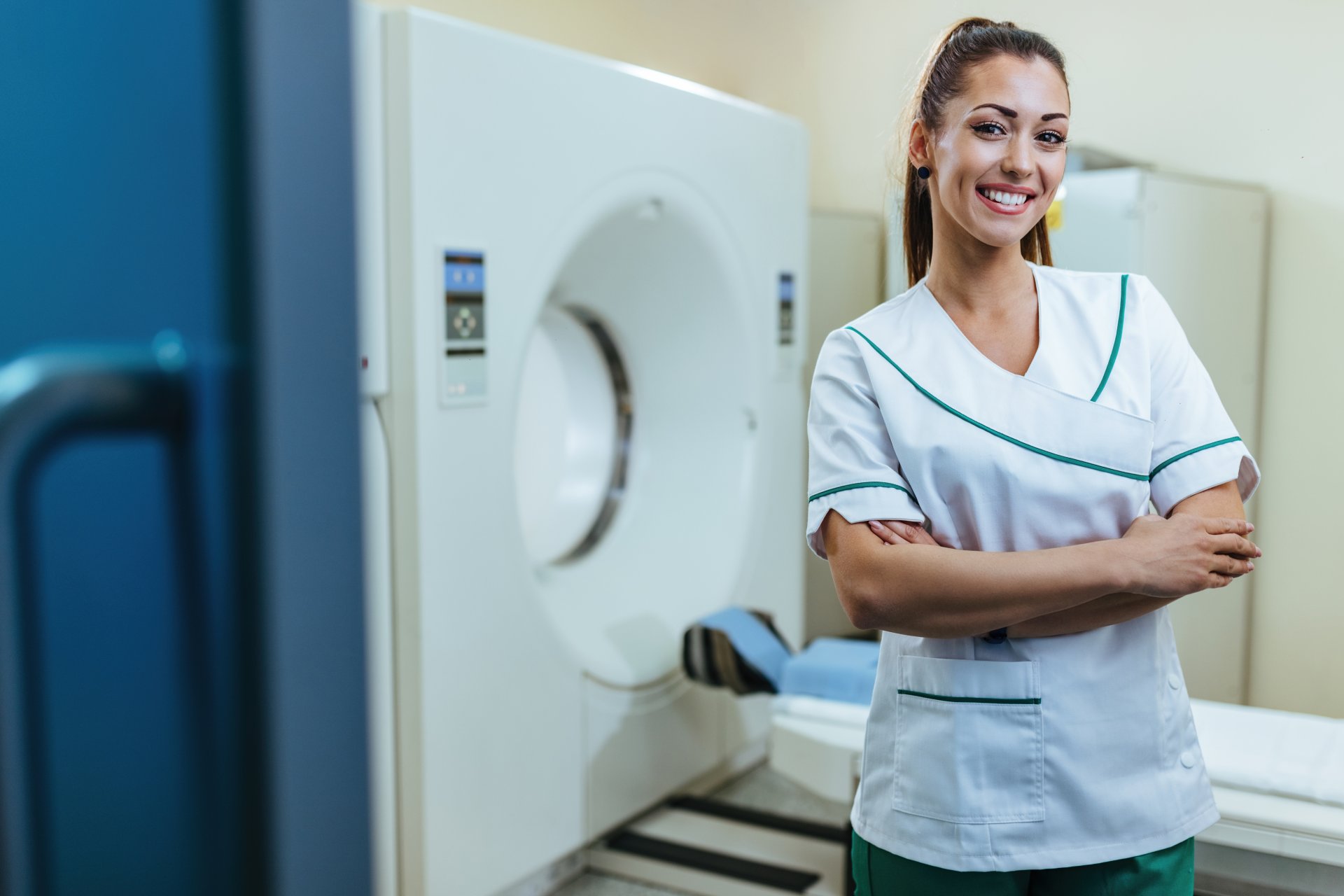 young-happy-doctor-standing-with-her-arms-crossed-mri-scanner-looking-camera